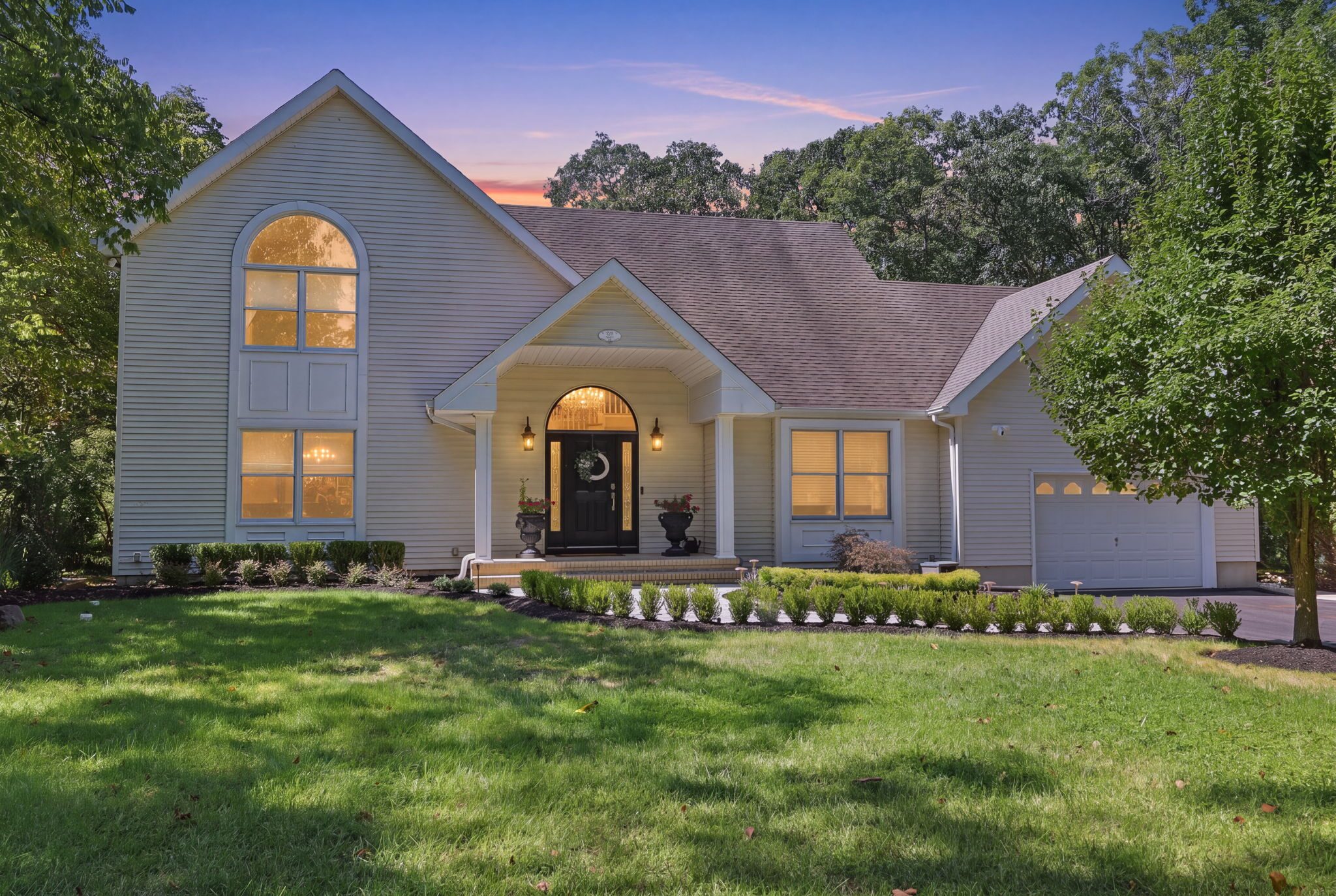 324 Jackson Mills Road at dusk — a Colonial home with warm interior lighting, framed by mature trees